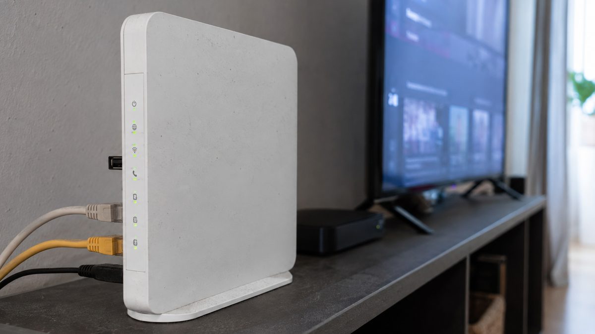 Home router with status lights on a shelf beside a television in a living room
